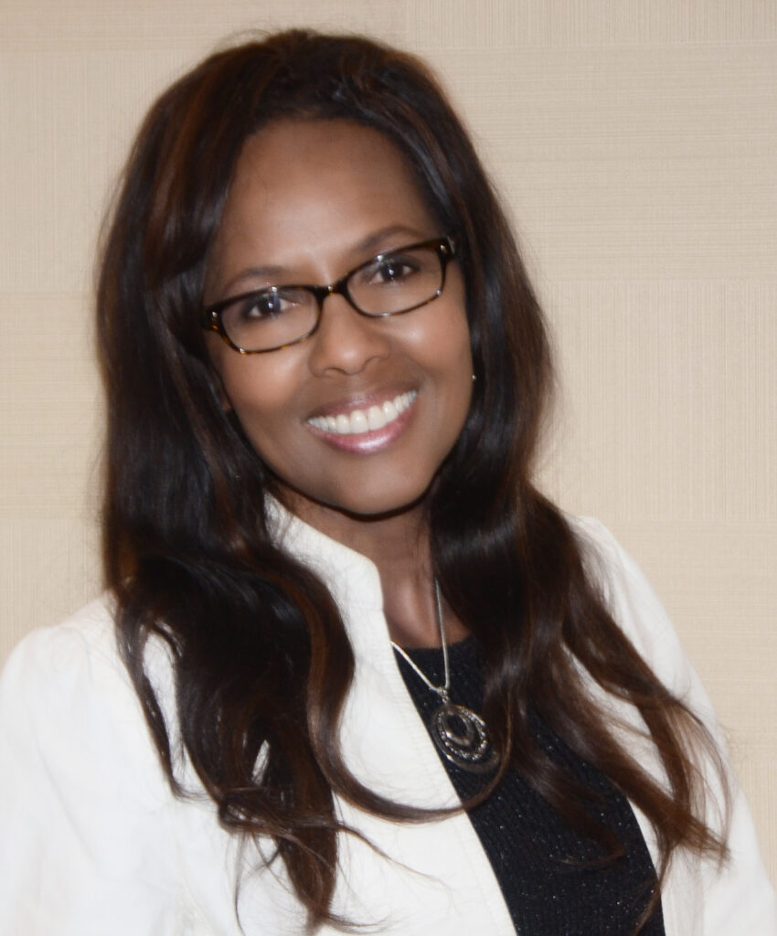 Yvette Long is an African American woman with long dark hair and glasses. She is wearing a white coat and black blouse.